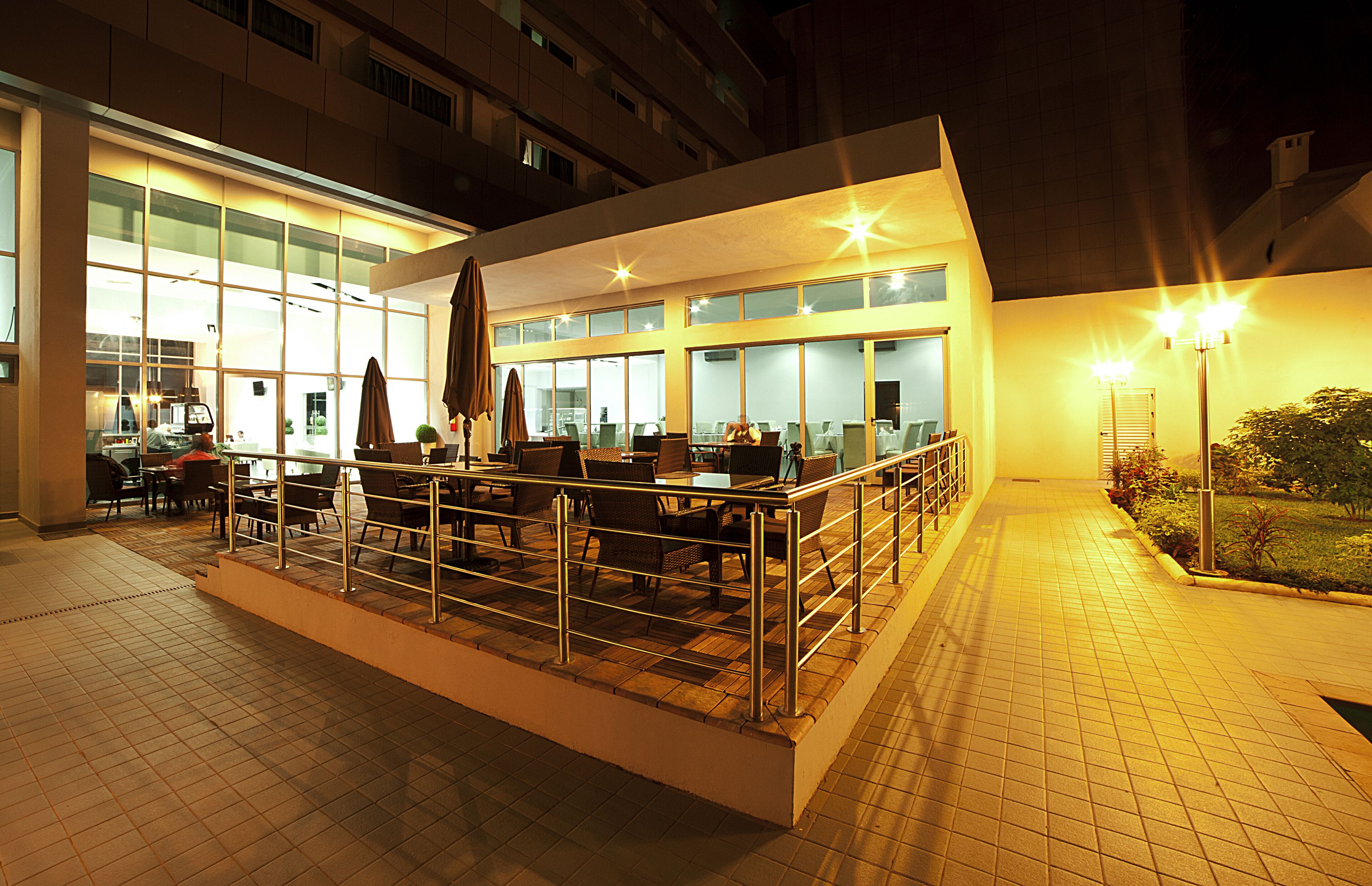 An outdoor seating area with tables and chairs, a covered section, and a building with large windows in the background.