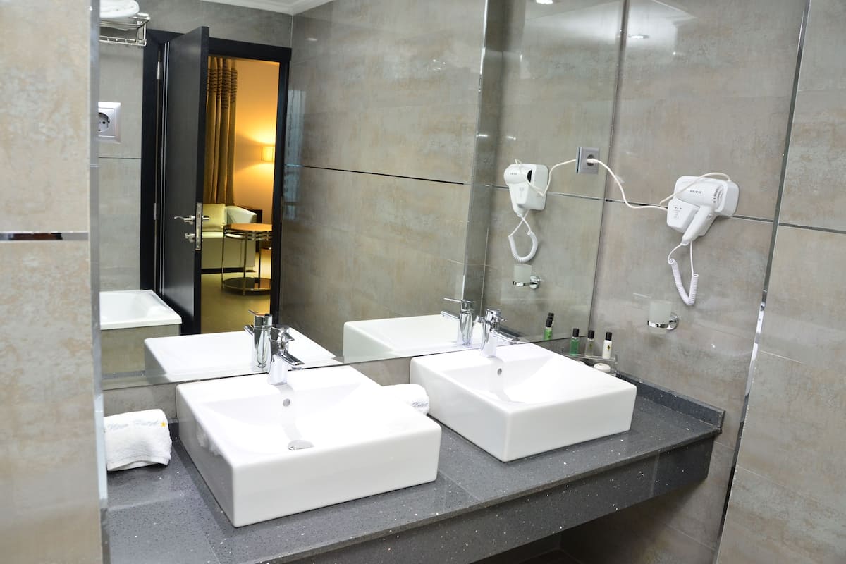 Uma casa de banho moderna com três lavatórios brancos, um espelho grande e um secador de cabelo na parede.