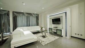 A modern living room with a white sectional sofa, a glass coffee table, and a flat-screen TV mounted on the wall. - New Hotel - Nampula (Nampula)