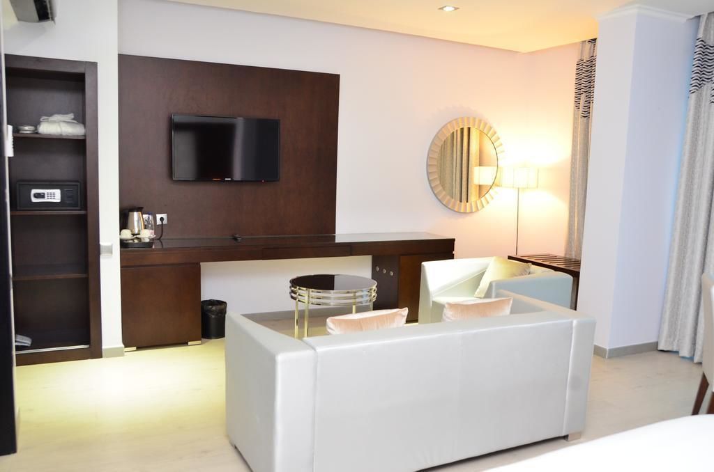 Une chambre d’hôtel dotée d’un téléviseur à écran plat fixé au mur, d’un miroir rond, d’un bureau avec une lampe et d’un coin salon comprenant un canapé et des fauteuils.