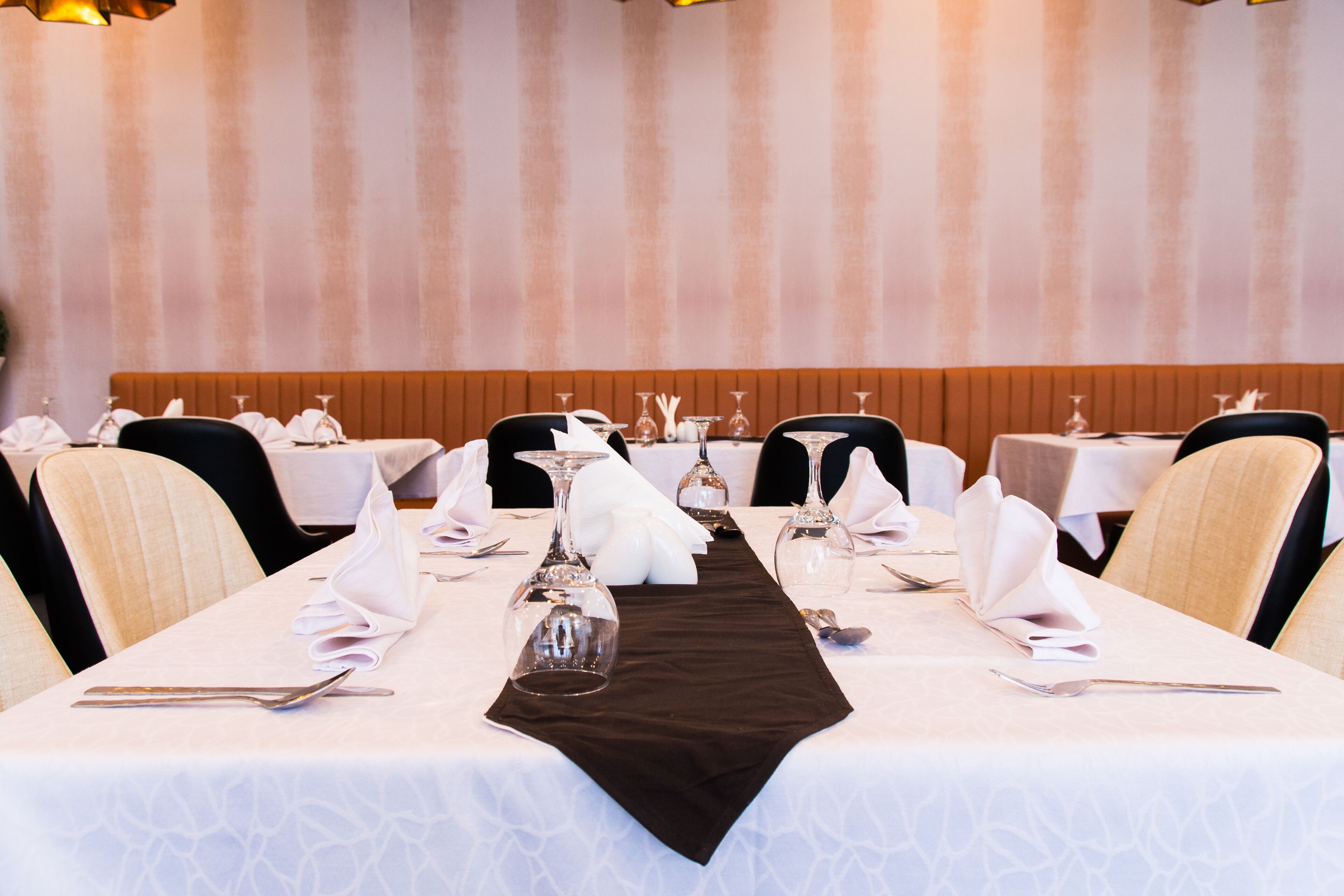 A dining area with tables set for a meal, featuring white tablecloths, neatly folded napkins, and wine glasses.