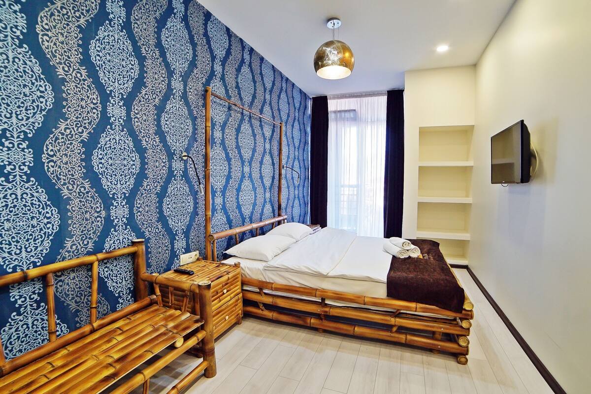 A room with a bed, a wooden bench, a TV, and a patterned wall.
