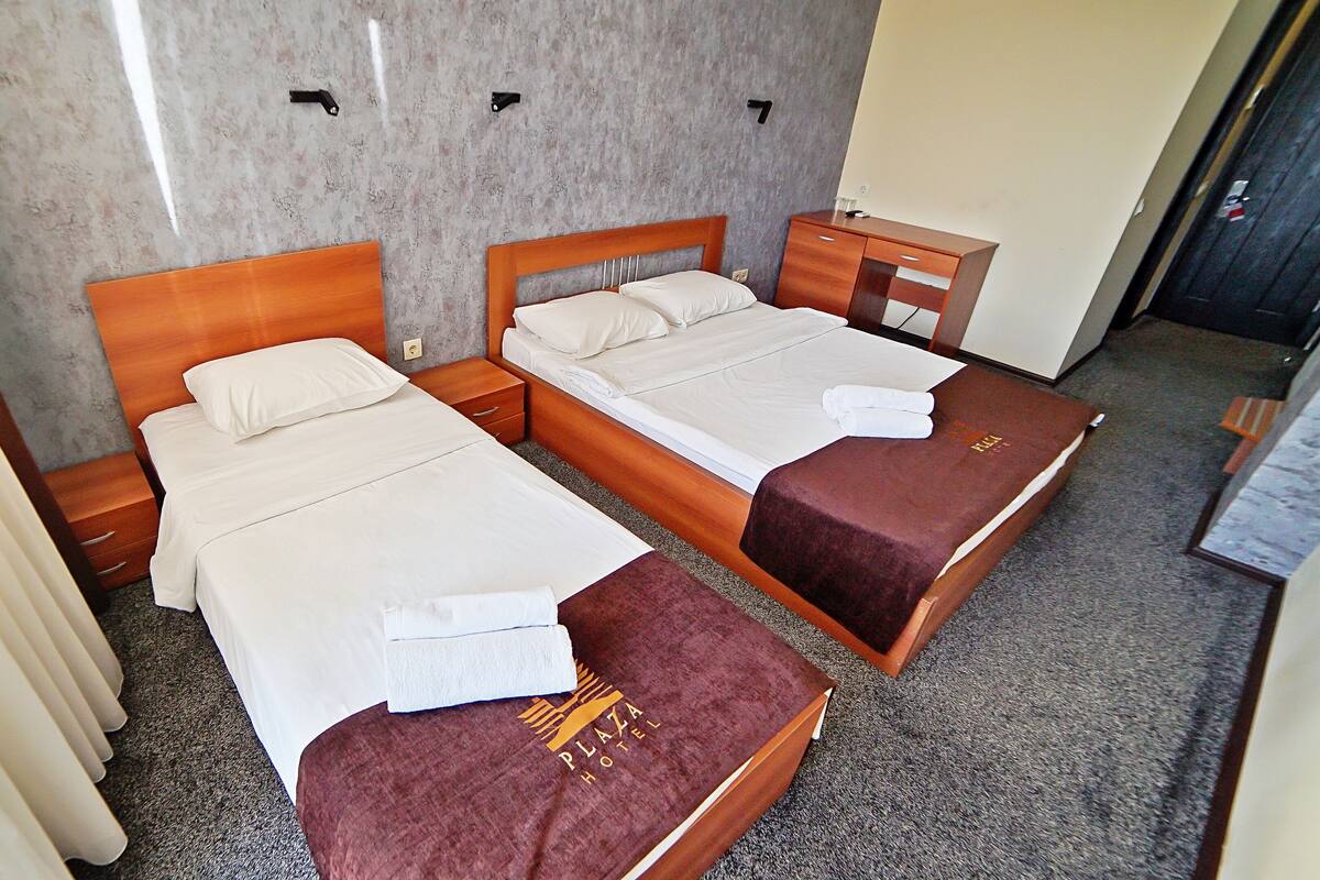 A hotel room with two single beds, a wooden headboard, a nightstand, and a small table with a towel.