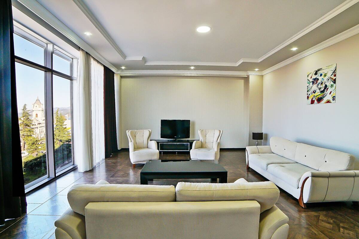 A spacious living room with a large window, a flat-screen TV, a sofa, and a coffee table.