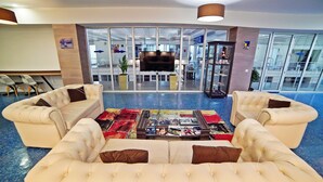 A lobby with a large, plush sofa set, a coffee table with magazines, and a television screen. - Mardi Plaza Hotel (Batumi)