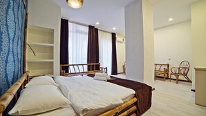 A hotel room with a bed, wooden headboard, and a large window with curtains. There are two chairs and a small table in the corner. - Mardi Plaza Hotel (Batumi)