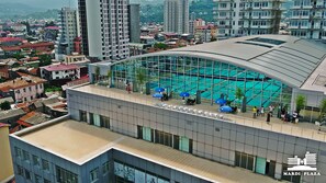 A modern building with a curved glass facade, a rooftop pool area with blue umbrellas, and a view of the surrounding cityscape. - Mardi Plaza Hotel (Batumi)