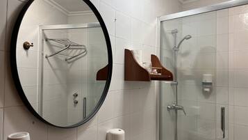 A bathroom with a round mirror, a glass-enclosed shower, a towel rack, and a soap dispenser.