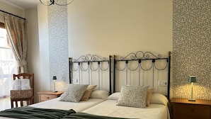 A double bed with a metal headboard, two bedside tables with lamps, a wooden chair with towels, and patterned wallpaper. - Las Casucas de Remoña (Camaleno)