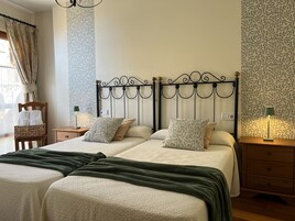 Una cama doble con cabecera de metal, dos mesitas de noche con lámparas, una silla de madera con toallas y papel tapiz estampado.