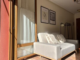 Una habitación con un sofá gris, suelo de madera, puerta de cristal y dos cuadros en la pared.