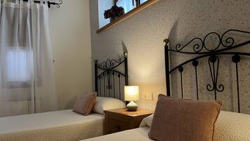 A bedroom with two beds, a nightstand, a lamp, and a window with a curtain.