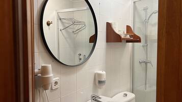 Un baño con un espejo redondo, un lavamanos, un inodoro y una ducha con mampara de vidrio.