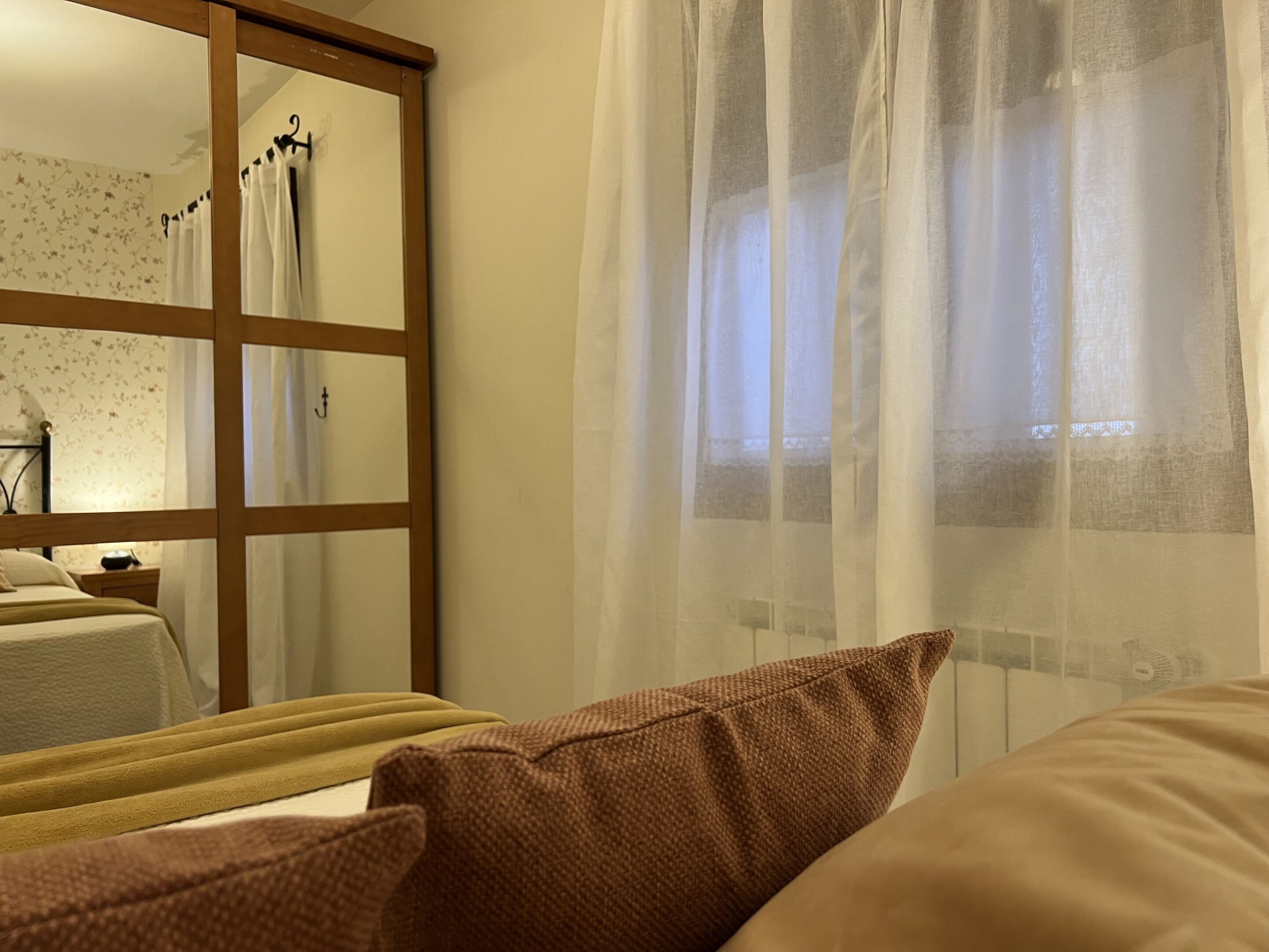 Un dormitorio con cama, mesita de noche, espejo y cortinas de encaje.