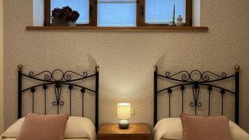 A bedroom with two beds, a nightstand with a lamp, and a window with a view.