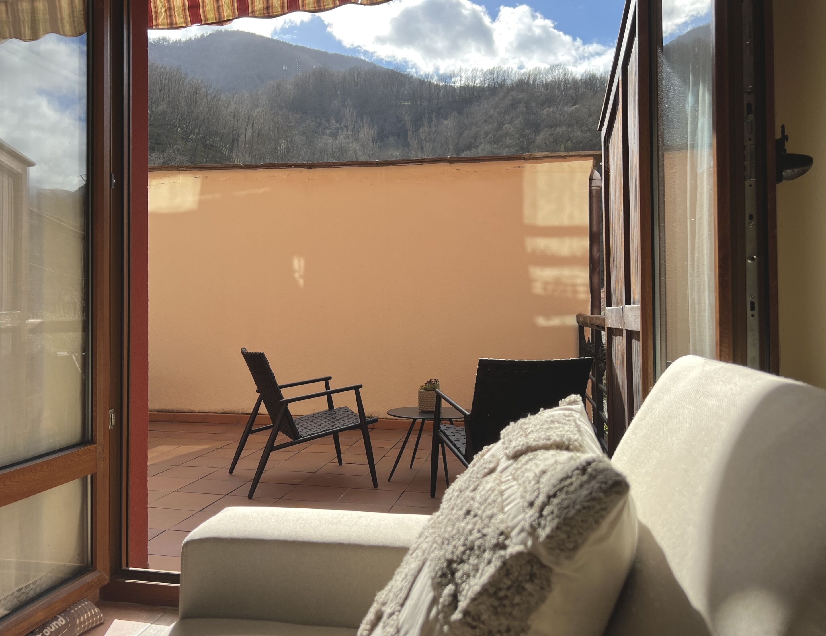 Un balcón con sofá, dos sillones y una mesita. Se ve una vista de la montaña a través de los ventanales.