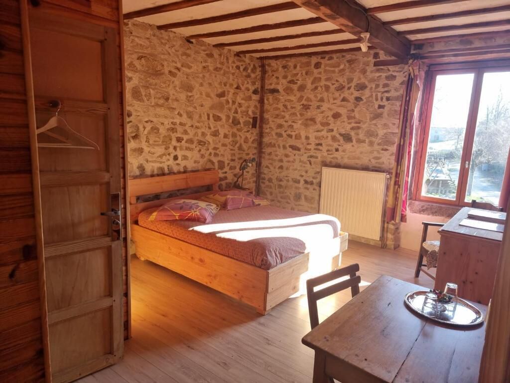 A rustic wooden room with a stone wall, a bed, a table with a tray, and a window with a view.