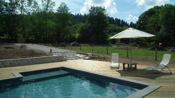 Une piscine avec une terrasse en bois, deux chaises longues et un parasol blanc.
