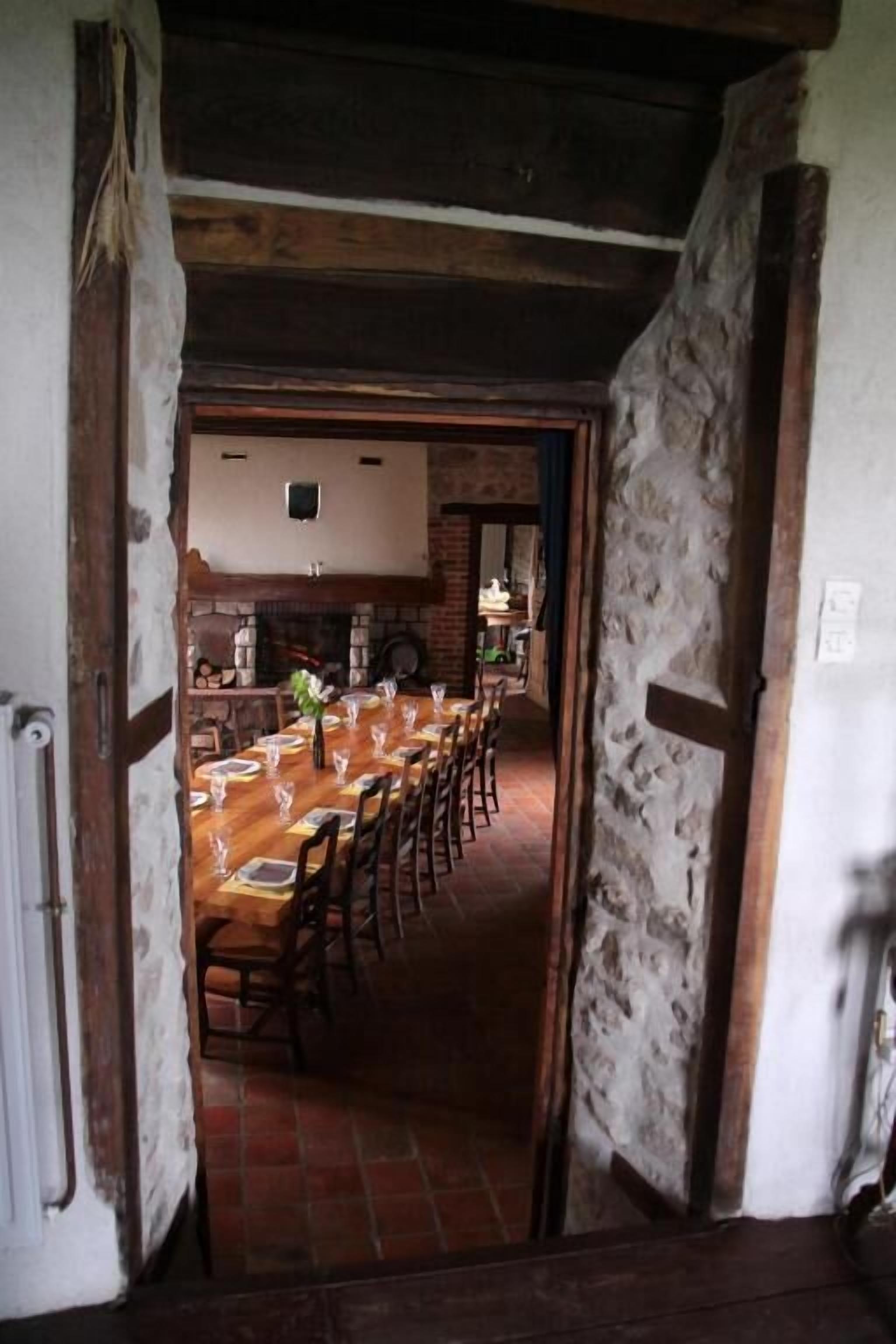 Ein rustikaler Essbereich mit einem langen Holztisch, gedeckt für eine Mahlzeit, der von Steinwänden und einer Holzbalkendecke gesäumt wird.