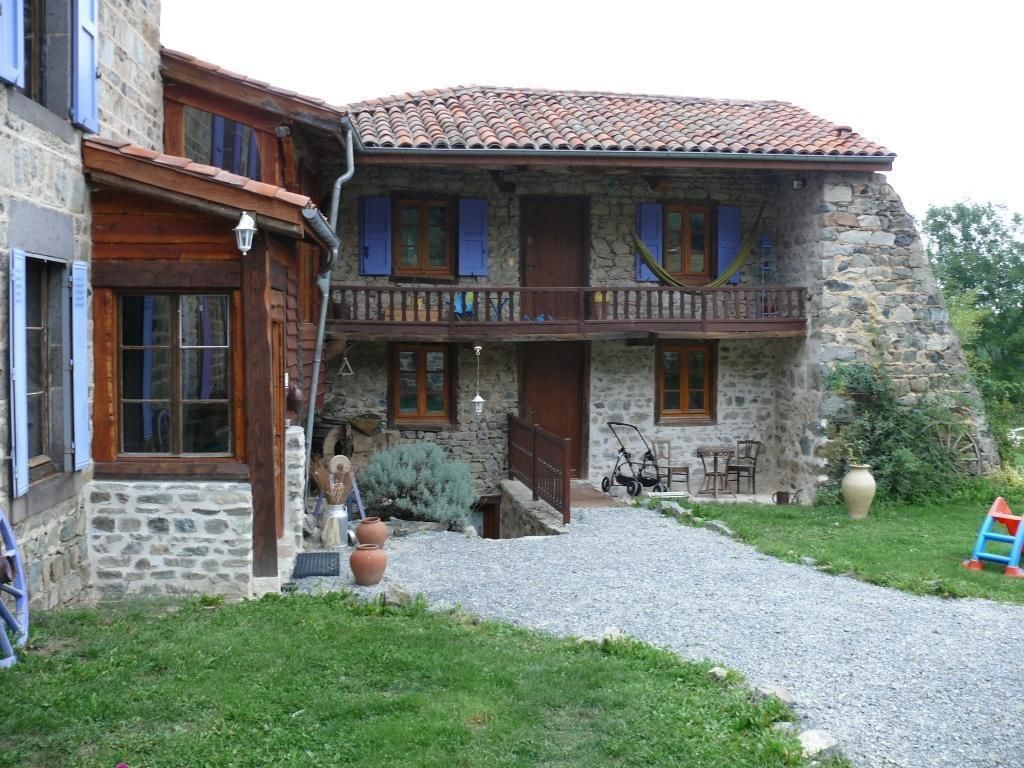 Un edificio de piedra con un balcón, camino de grava y mobiliario exterior.