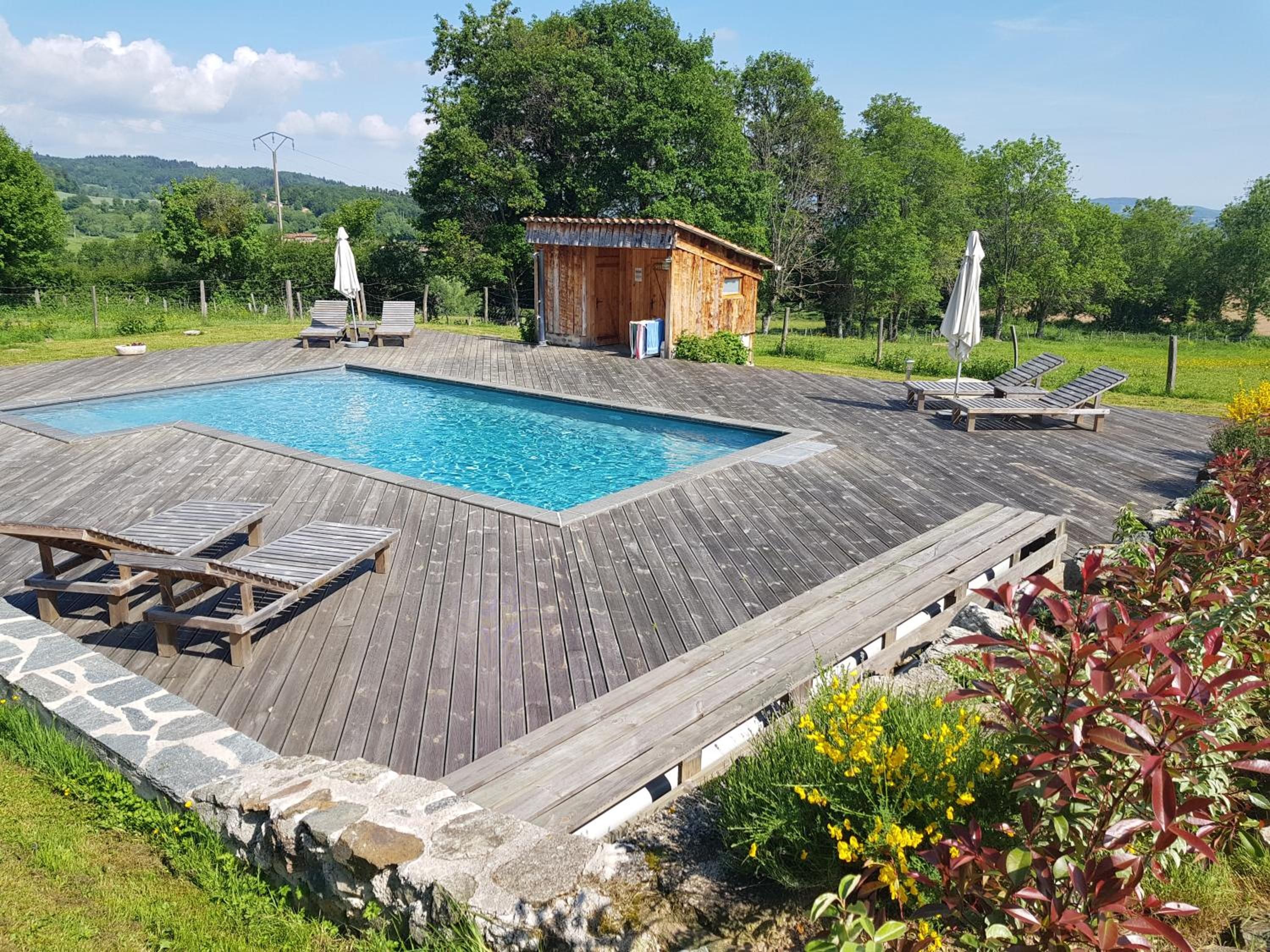 Una terraza de madera con piscina, sillones de descanso y una pequeña construcción de madera.