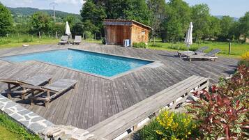 Una terraza de madera con piscina, sillones de descanso y una pequeña construcción de madera.