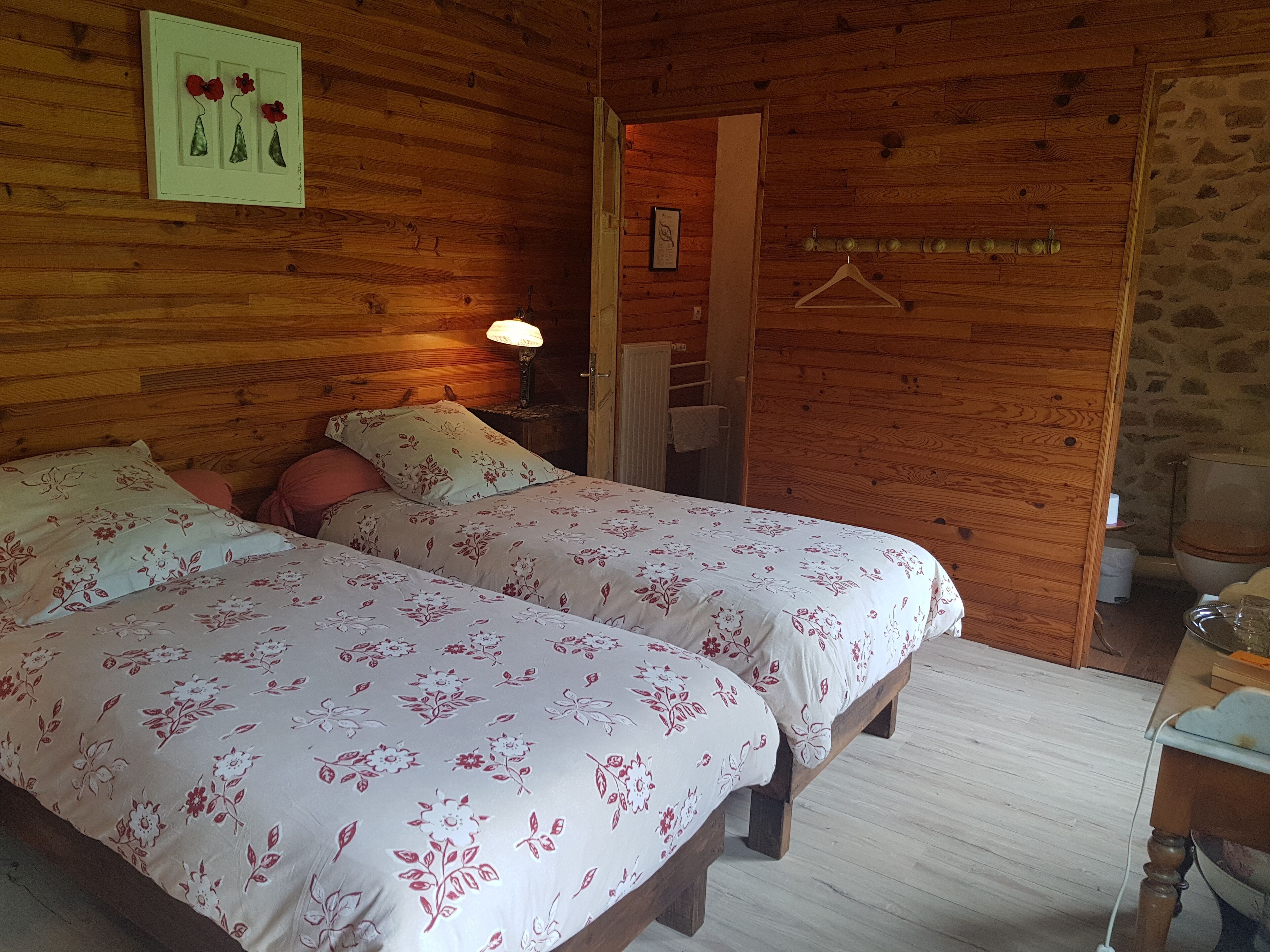 A wooden cabin room with two beds, a hanging light, and a stone wall.