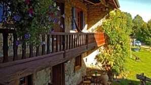 A rustic stone building with a wooden balcony, surrounded by greenery and a well-maintained lawn.