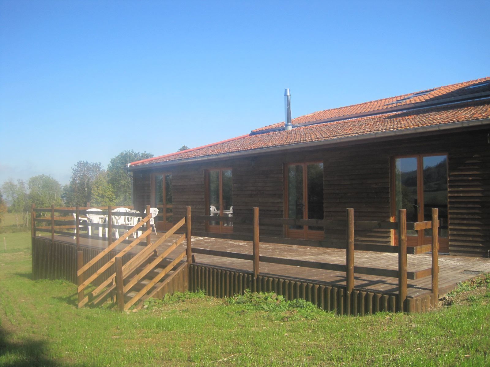 A wooden cabin with a tiled roof, a deck with outdoor furniture, and a fenced area.