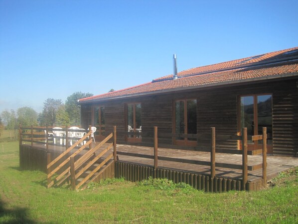 A wooden cabin with a tiled roof, a deck with outdoor furniture, and a fenced area.