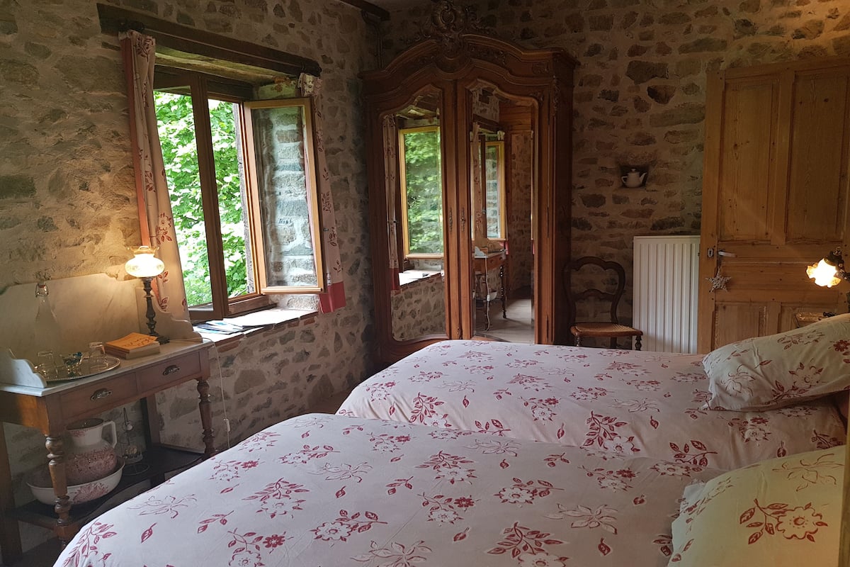 Un dormitori amb paret de pedra, armari de fusta i llit amb roba de llit floral.