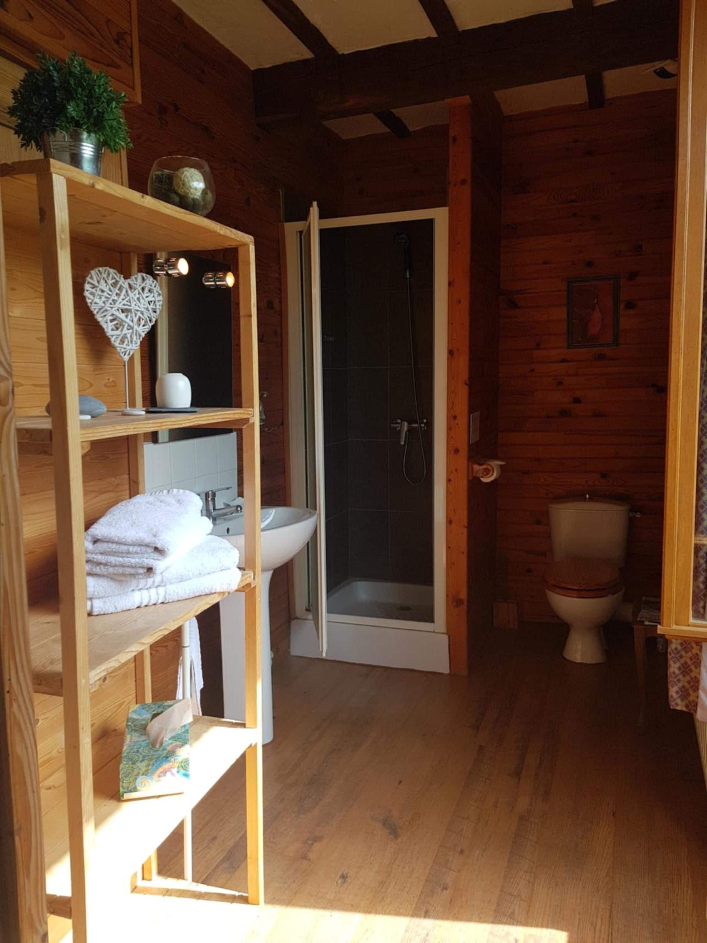 A wooden cabin bathroom with a shower, toilet, and a shelf with towels.