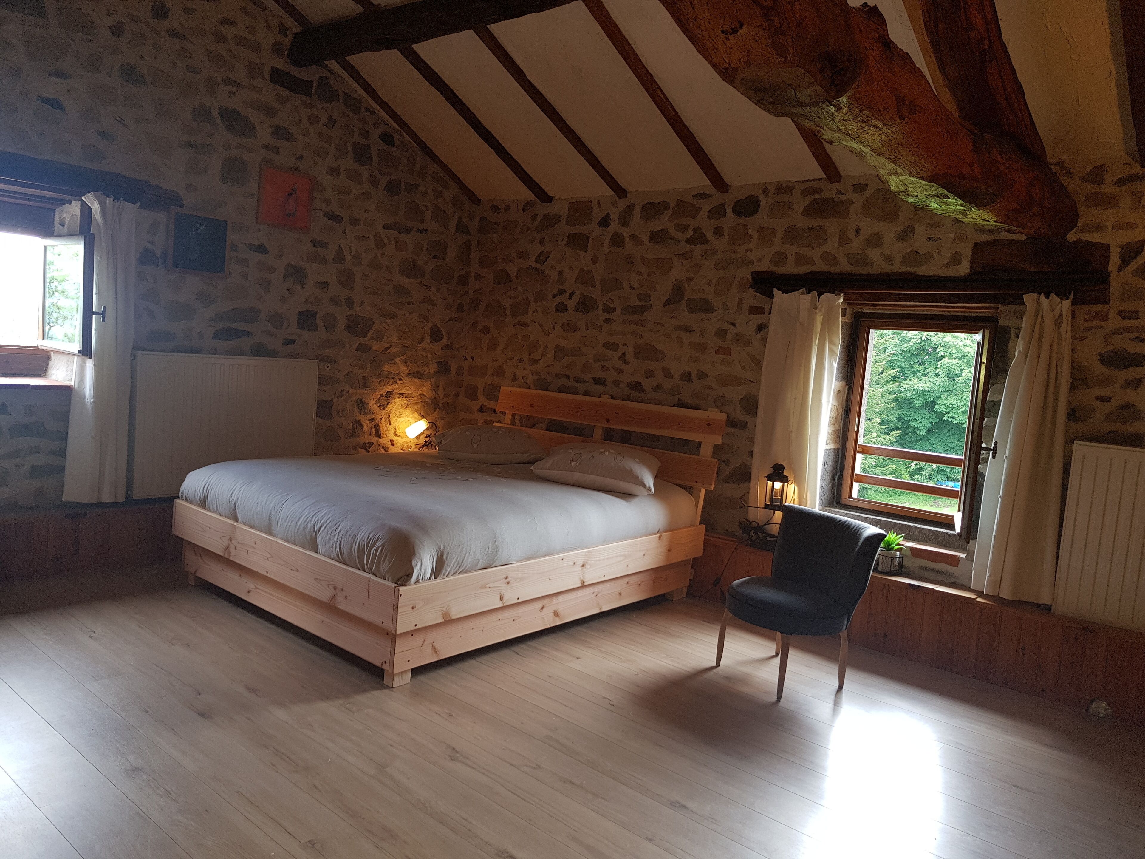 Ein Schlafzimmer mit Steinwand, einem Holzbett, einem Stuhl und einem Fenster mit Vorhängen.