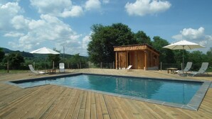 A wooden deck with a swimming pool, lounge chairs, and umbrellas.