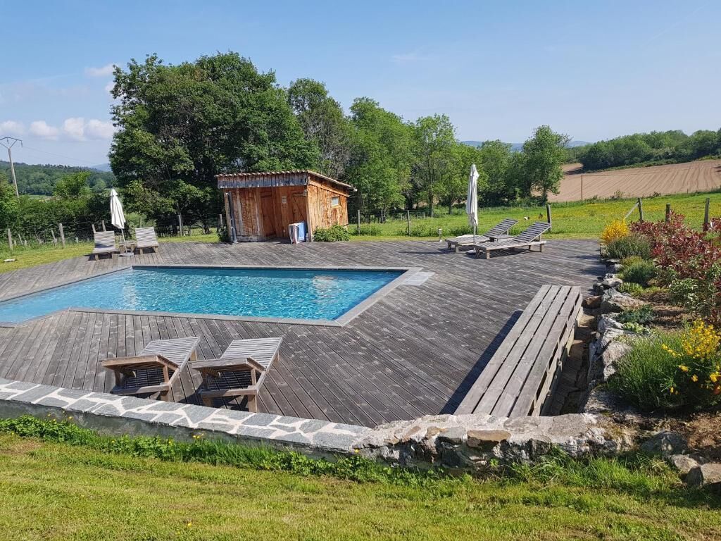 Piscina rectangular con muelle de madera y sillas reclinables, rodeada por un muro de piedra y vegetación.