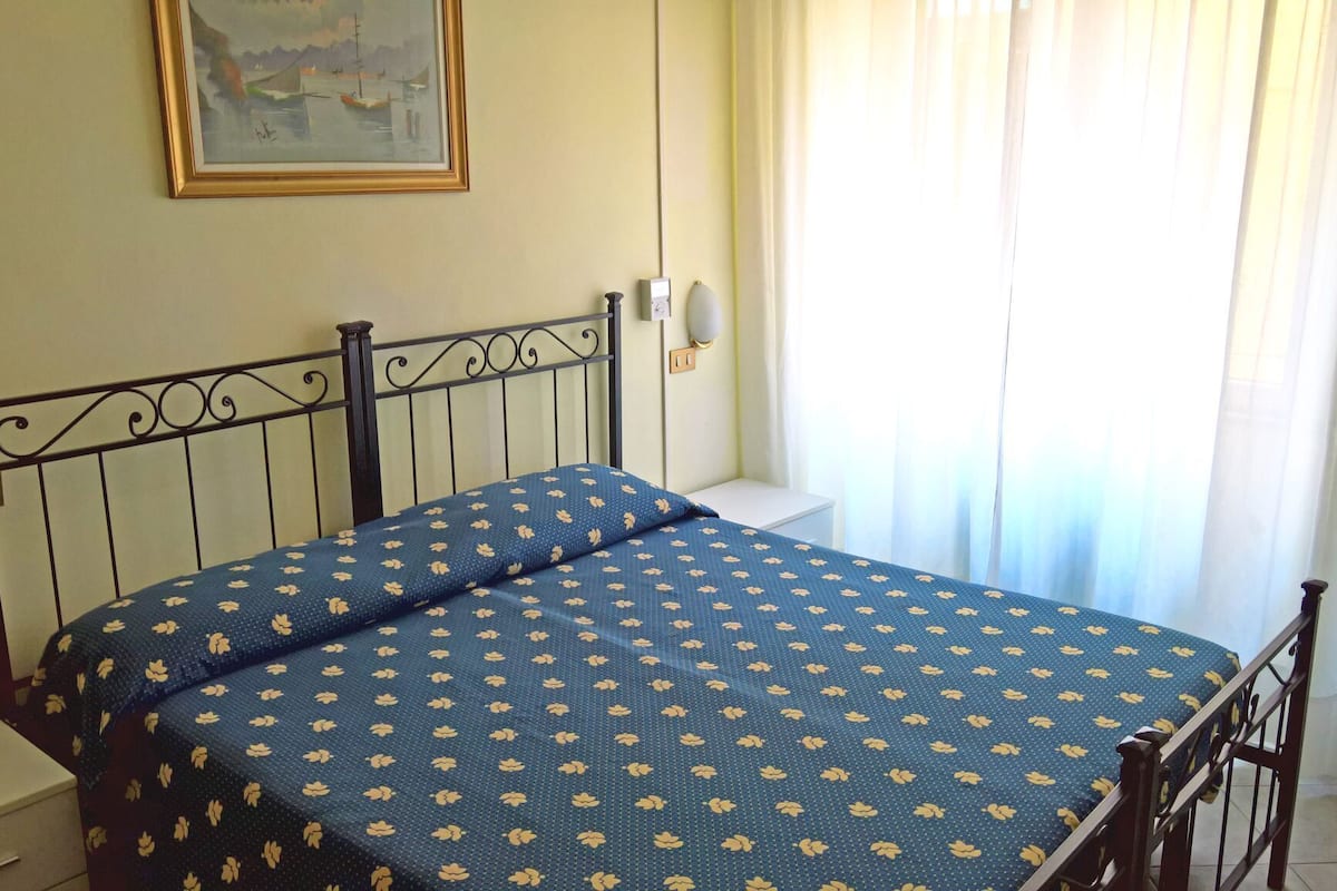 Une pièce avec un lit, un tableau au mur et une fenêtre avec des rideaux.