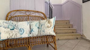Una cama de mimbre con un cojín de temática marina, una escalera con baranda morada y un cuadro de una jirafa en la pared.