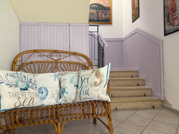A wicker bed with a pillow featuring a sea theme, a staircase with a purple railing, and a painting of a giraffe on the wall. - Albergo Golfo (Follonica)