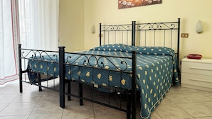 Una cama con estructura metálica y ropa de cama floral, un cuadro en la pared y una mesita de noche con una lámpara.