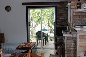 A room with a bed, a small table, a TV, and a sliding glass door leading to an outdoor area with chairs and a table. - Costas Hostel Action (Tseri)