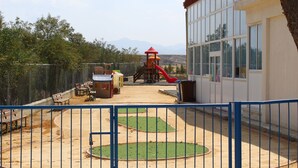 A playground with a slide and climbing structures, surrounded by benches and a fenced area. - Costas Hostel Action (Tseri)