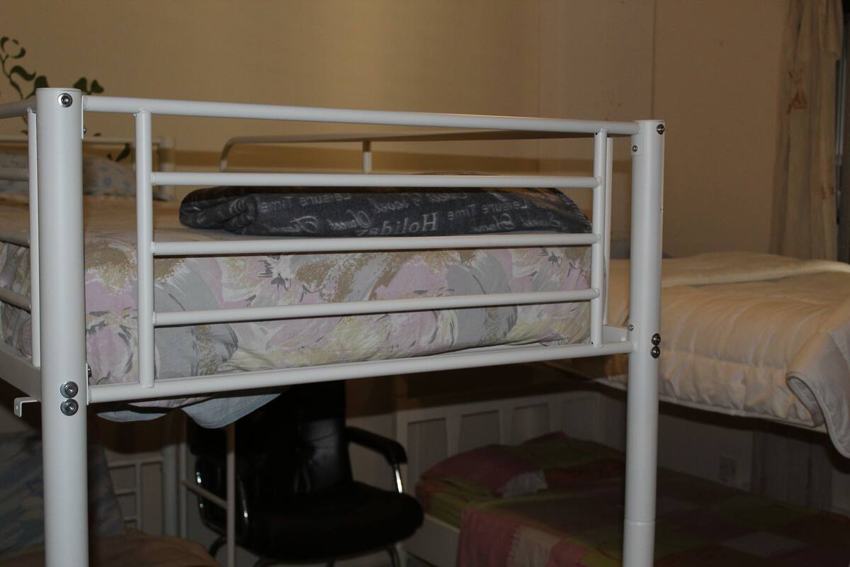 A bunk bed with a desk underneath, a chair, and a bed with a floral bedspread.