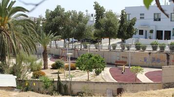 Parque con cancha de baloncesto, palmeras y un parque infantil.
