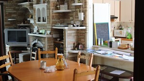 A kitchen with a brick wall, wooden cabinets, a dining table with chairs, a microwave, and a television. - Costas Hostel Action (Tseri)