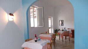 A dining area with tables covered in white tablecloths, wooden chairs, and a tiled floor. - B&B Porta di Suso (Camerota)