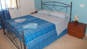 A single bed with a blue checkered bedspread, two bedside tables with lamps, and a window with curtains. - B&B Porta di Suso (Camerota)