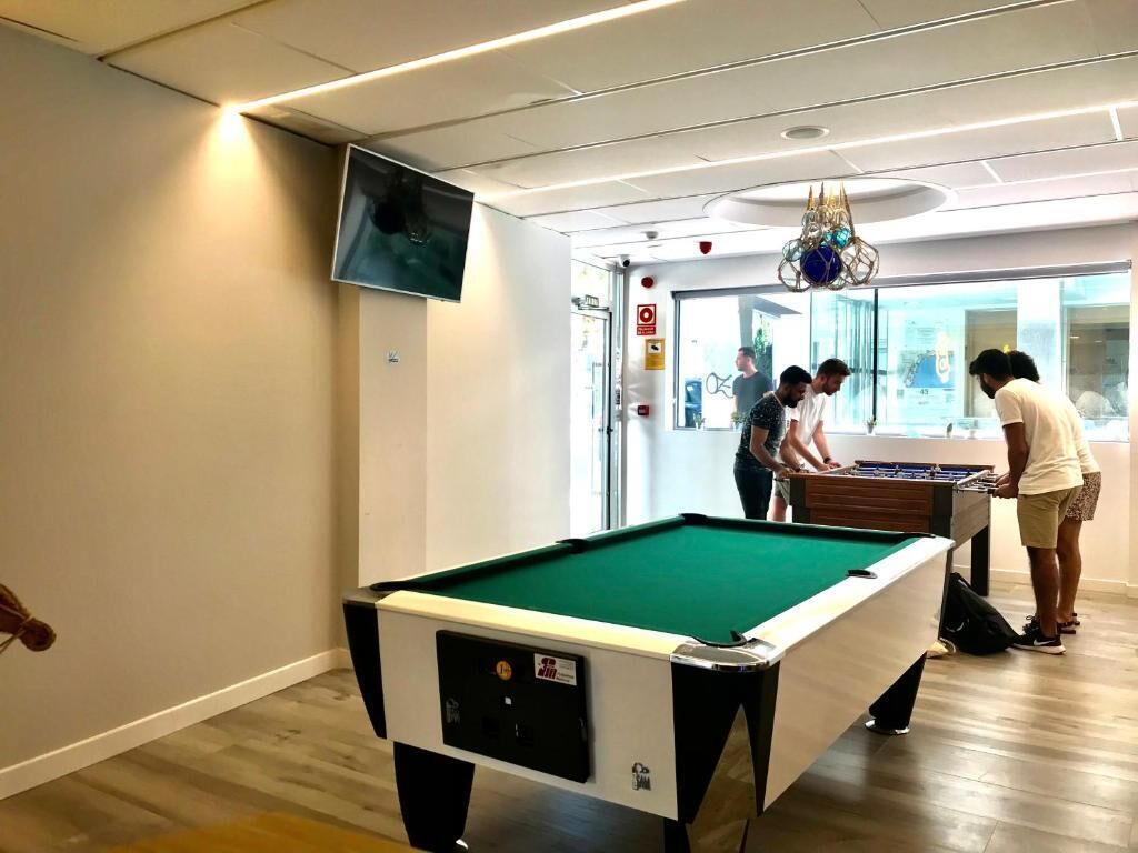 A pool table in a room with a television mounted on the wall, a chandelier, and a door with a sign.