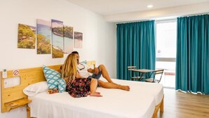 Un dormitorio con una cama, cabecera de madera, una mesita y una silla. Hay tres cuadros enmarcados en la pared.