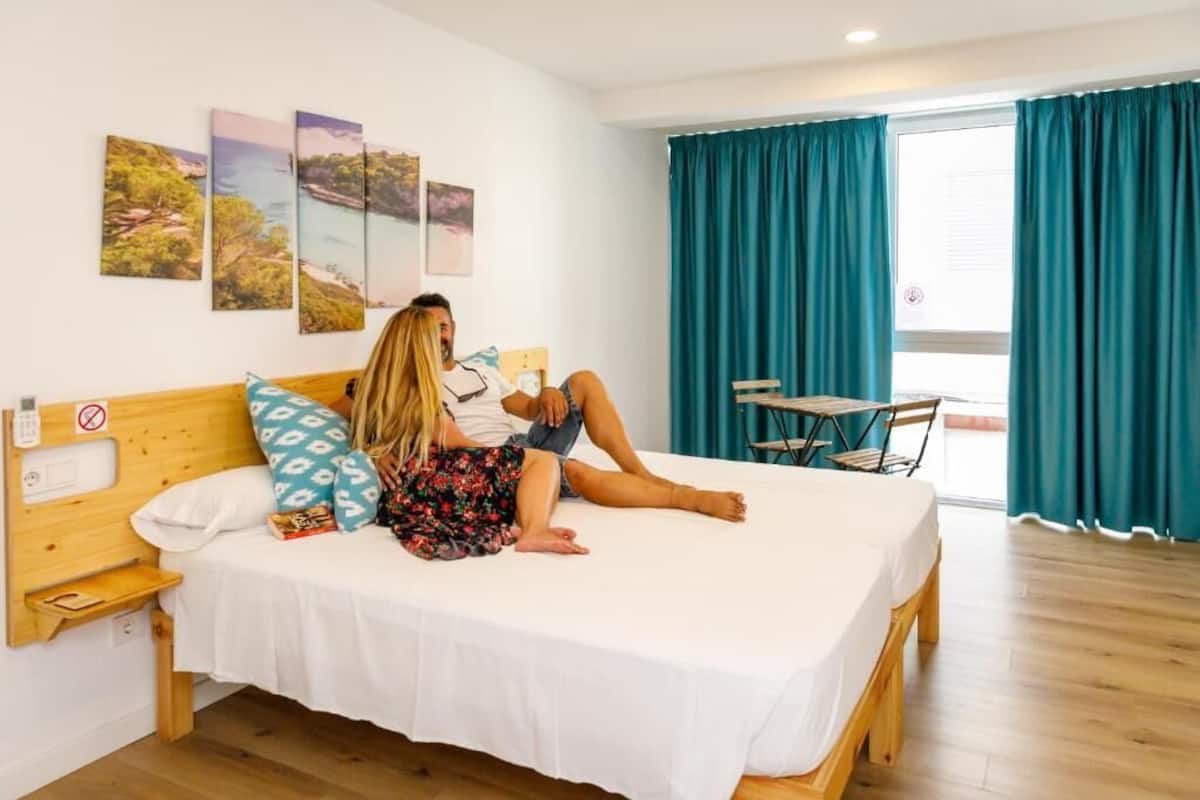 Un dormitorio con una cama, cabecera de madera, una mesita y una silla. Hay tres cuadros enmarcados en la pared.