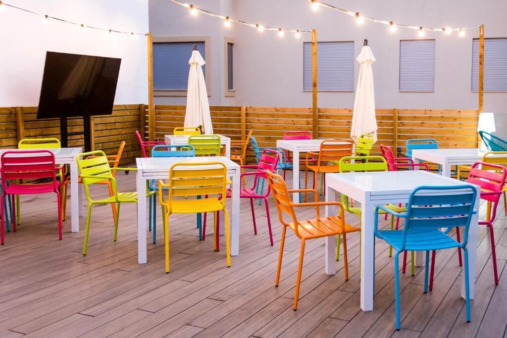 Un espace de restauration intérieur, bien éclairé, avec des chaises et des tables aux couleurs vives, des guirlandes lumineuses et un écran de télévision.